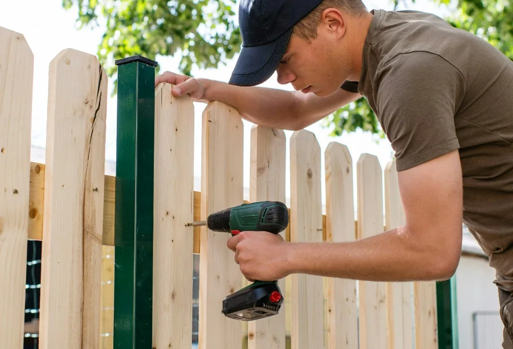 Handyman using a cordless drill to build a wooden garden fence in Austria